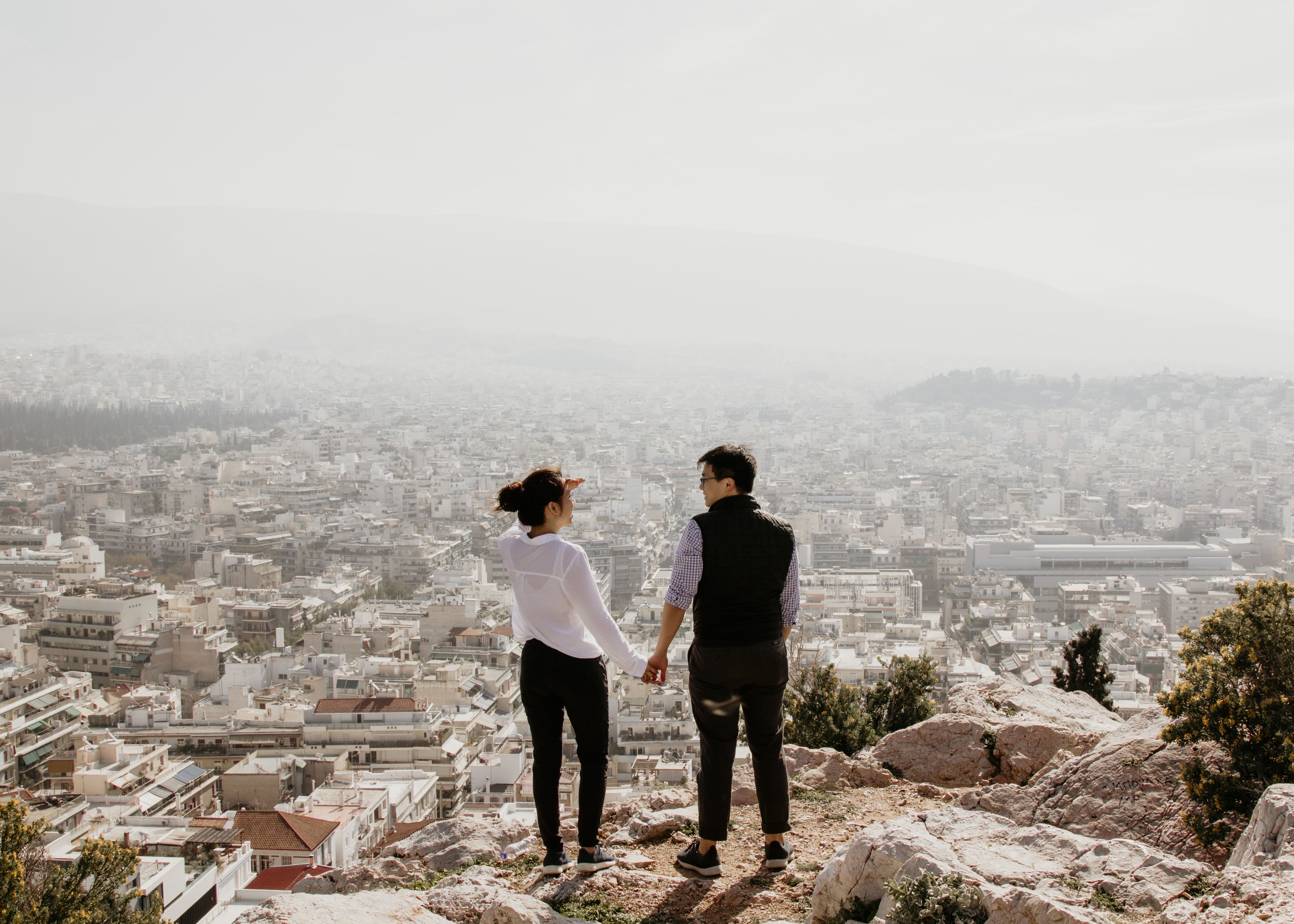 man and woman holding their hands together while standing on top of cliff